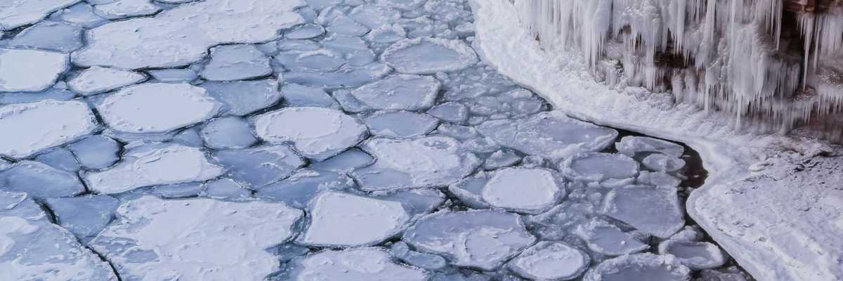 A view of ice-covered water with icicles forming on a nearby cliff