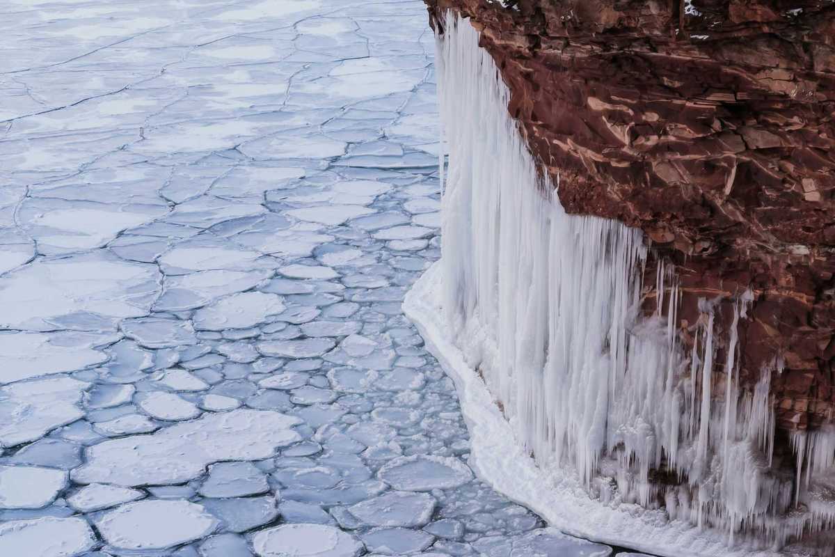 A view of ice-covered water with icicles forming on a nearby cliff