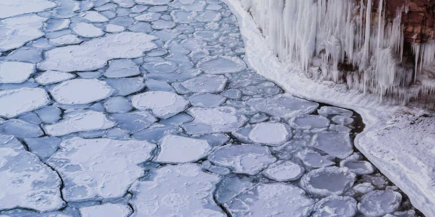A view of ice-covered water with icicles forming on a nearby cliff