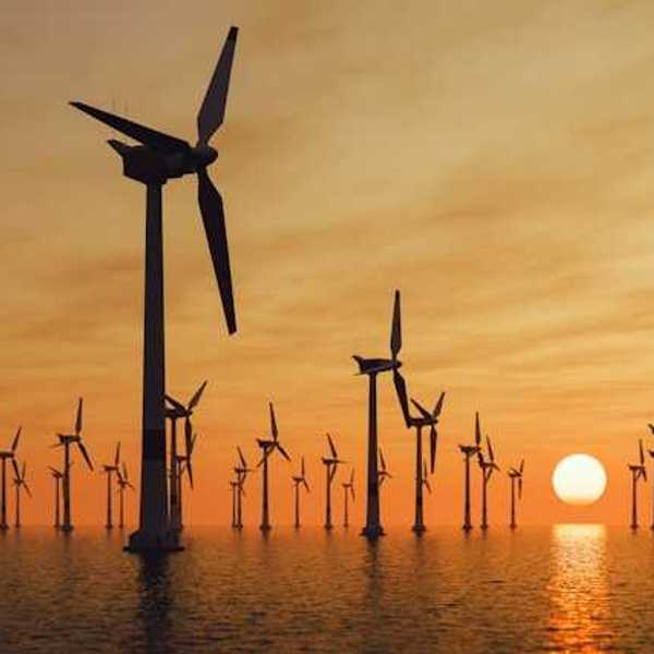 A view of many offshore wind turbines with the setting sun in the distance