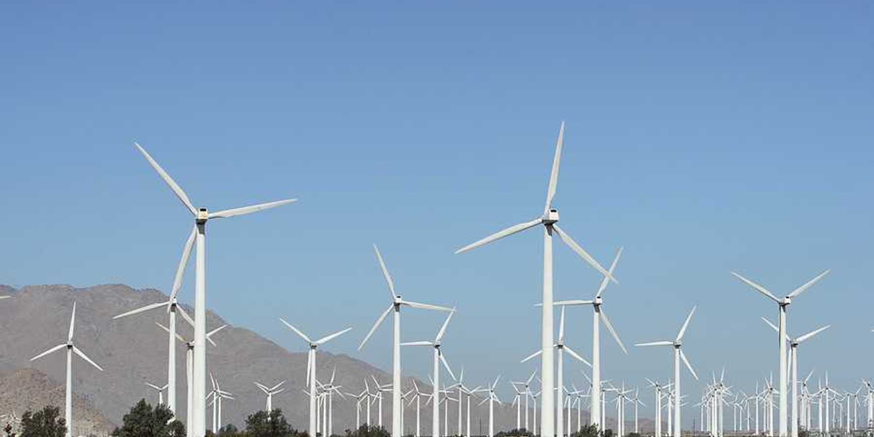 A view of multiple white wind turbines with dry mountains in the background