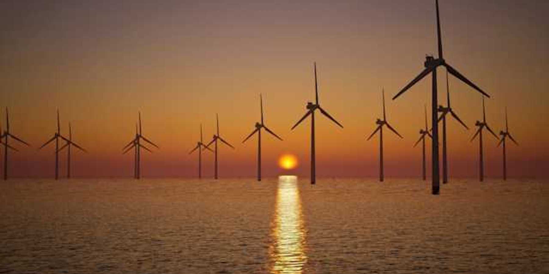 A view of offshore wind turbines with the setting sun in the distance