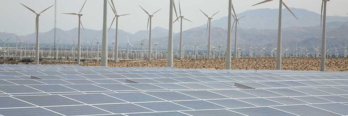 A view of solar panels and wind turbines with mountains in the background