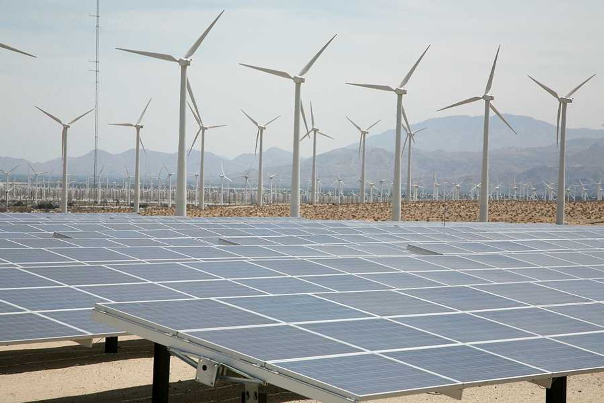 A view of solar panels and wind turbines with mountains in the background