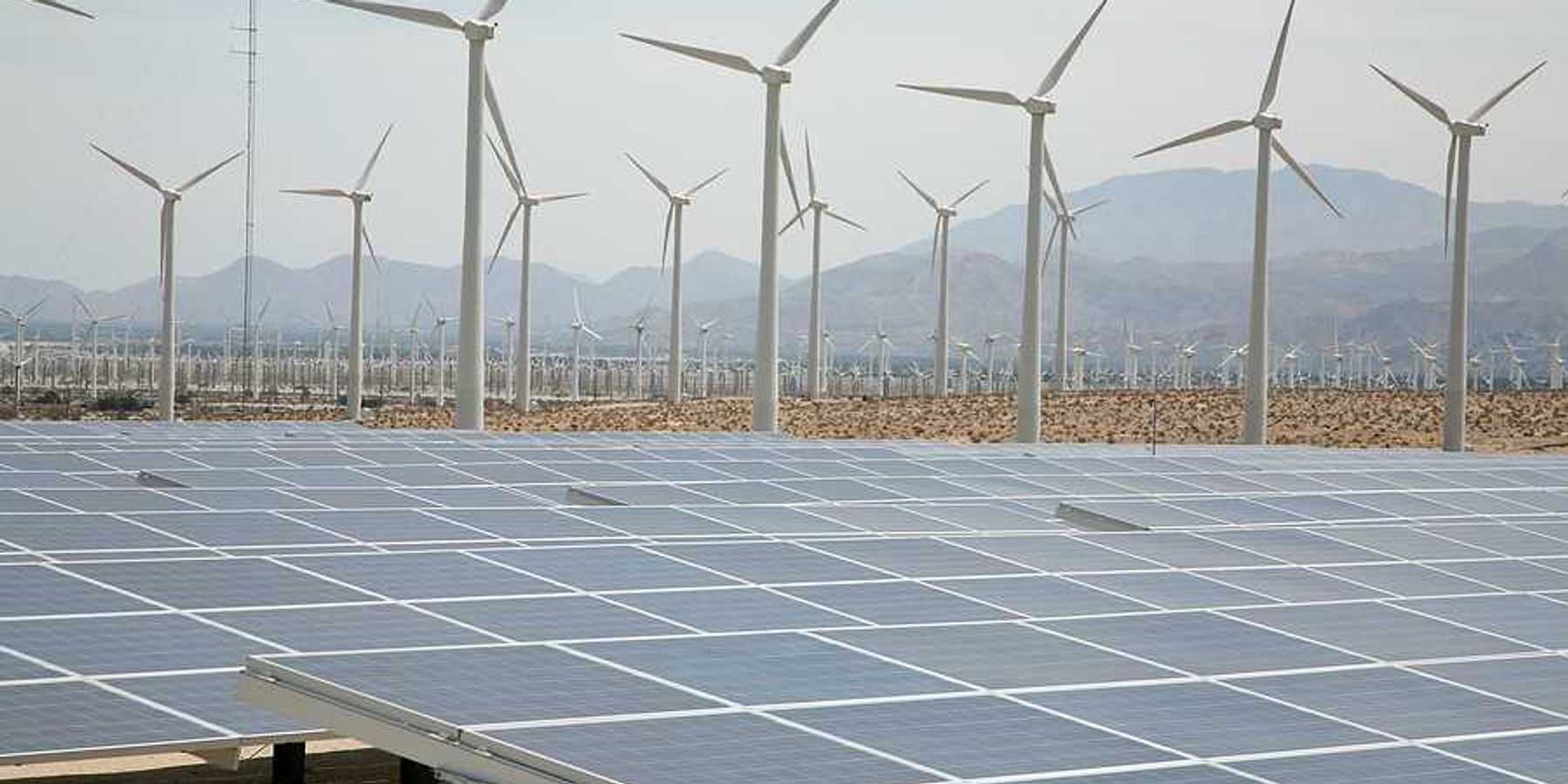 A view of solar panels and wind turbines with mountains in the background