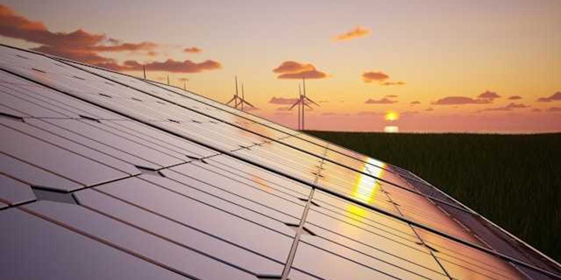 A view of solar panels and wind turbines with the sunset in the distance
