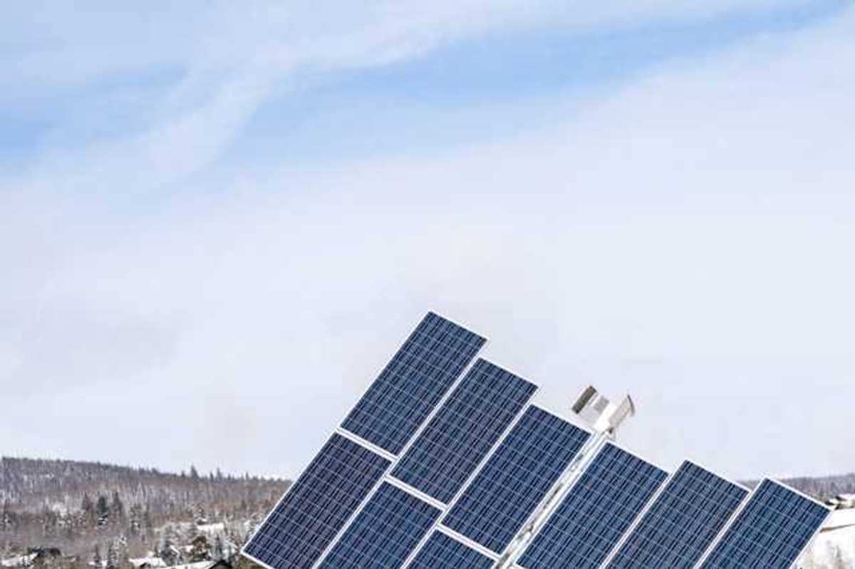 A view of solar panels with snow-covered hills behind them