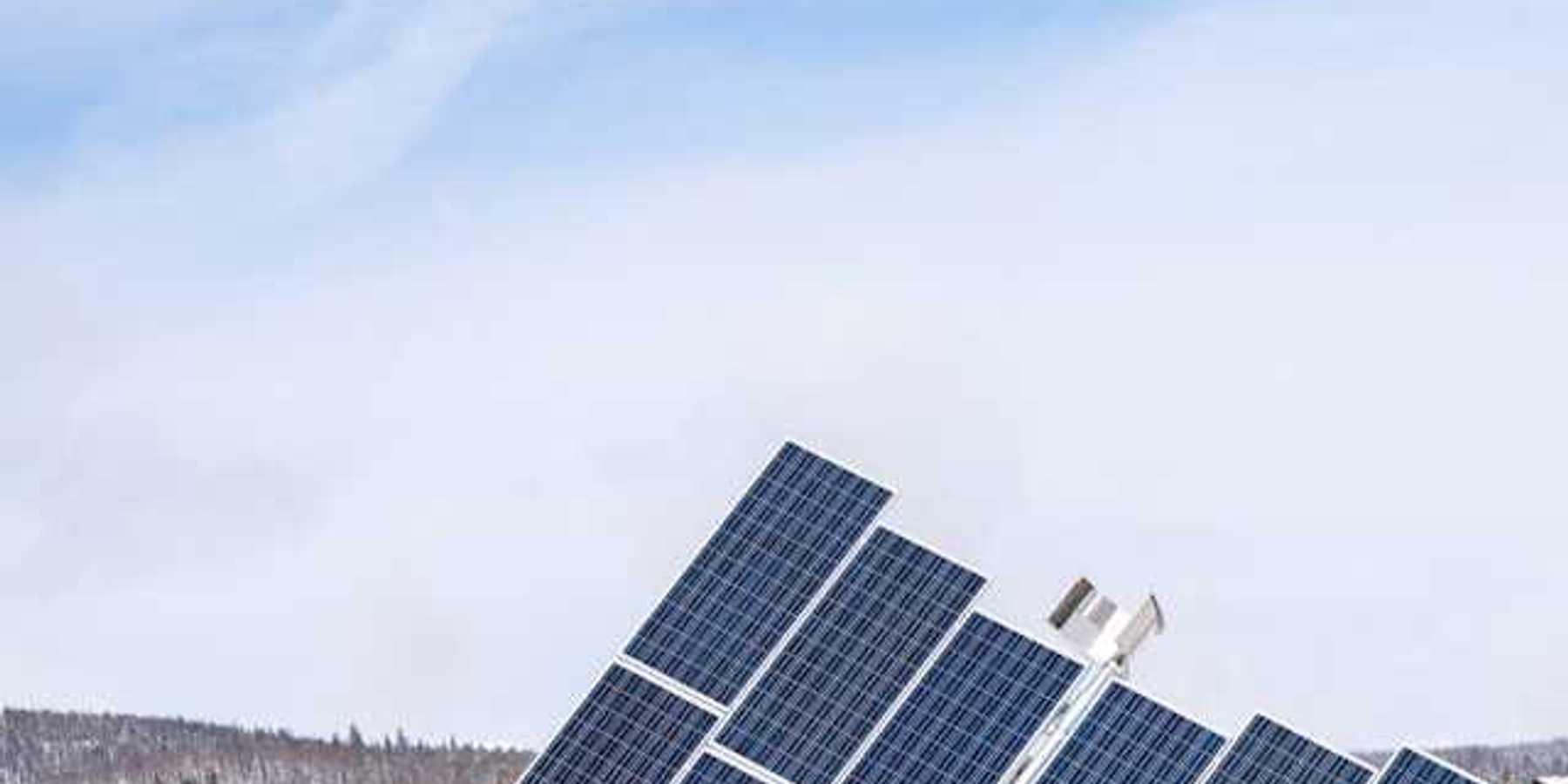 A view of solar panels with snow-covered hills behind them