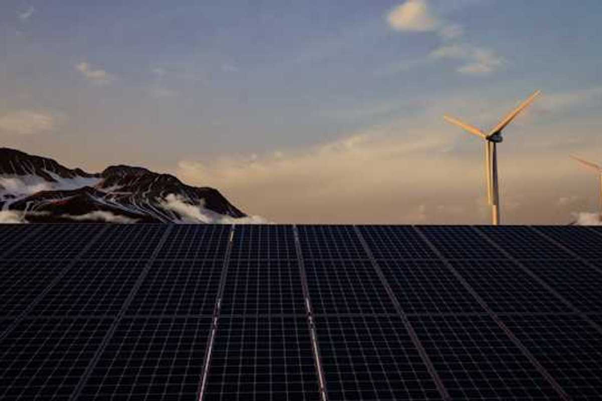 A view of solar panels with wind turbines and mountains in the background