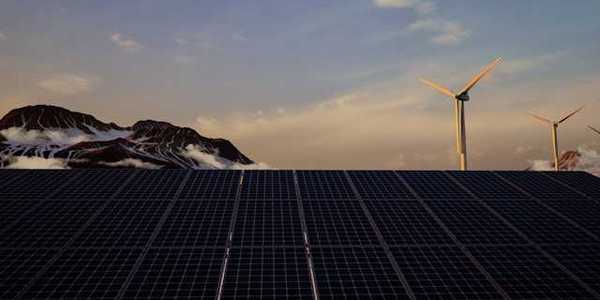 A view of solar panels with wind turbines and mountains in the background