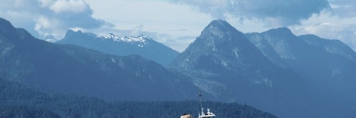 A view of tall mountains with water and a tugboat in the foreground