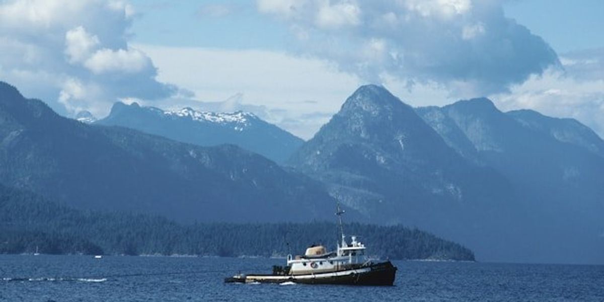 A view of tall mountains with water and a tugboat in the foreground