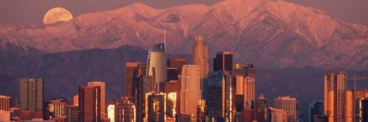 A view of the Denver skyline at dusk with the moon rising behind the mountains