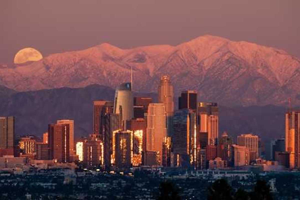 A view of the Denver skyline at dusk with the moon rising behind the mountains