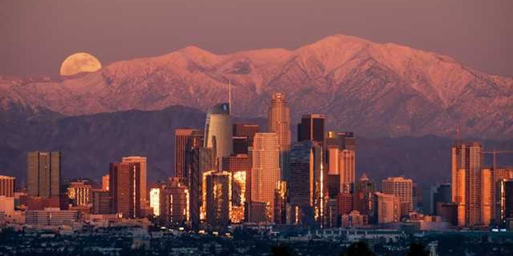 A view of the Denver skyline at dusk with the moon rising behind the mountains