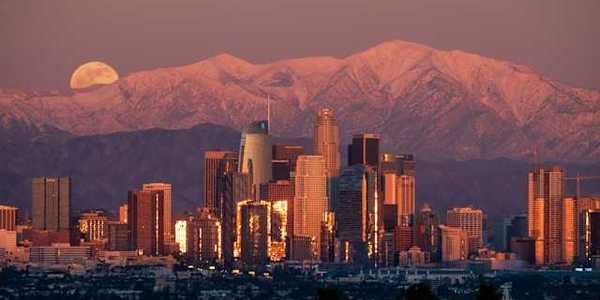 A view of the Denver skyline at dusk with the moon rising behind the mountains