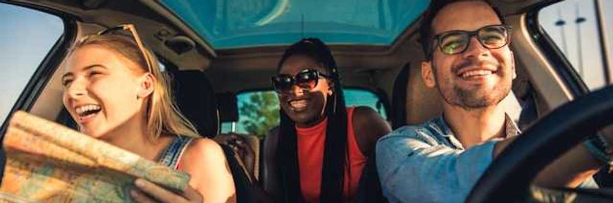 A view of the interior of a car with three laughing people, one of whom is looking at a map