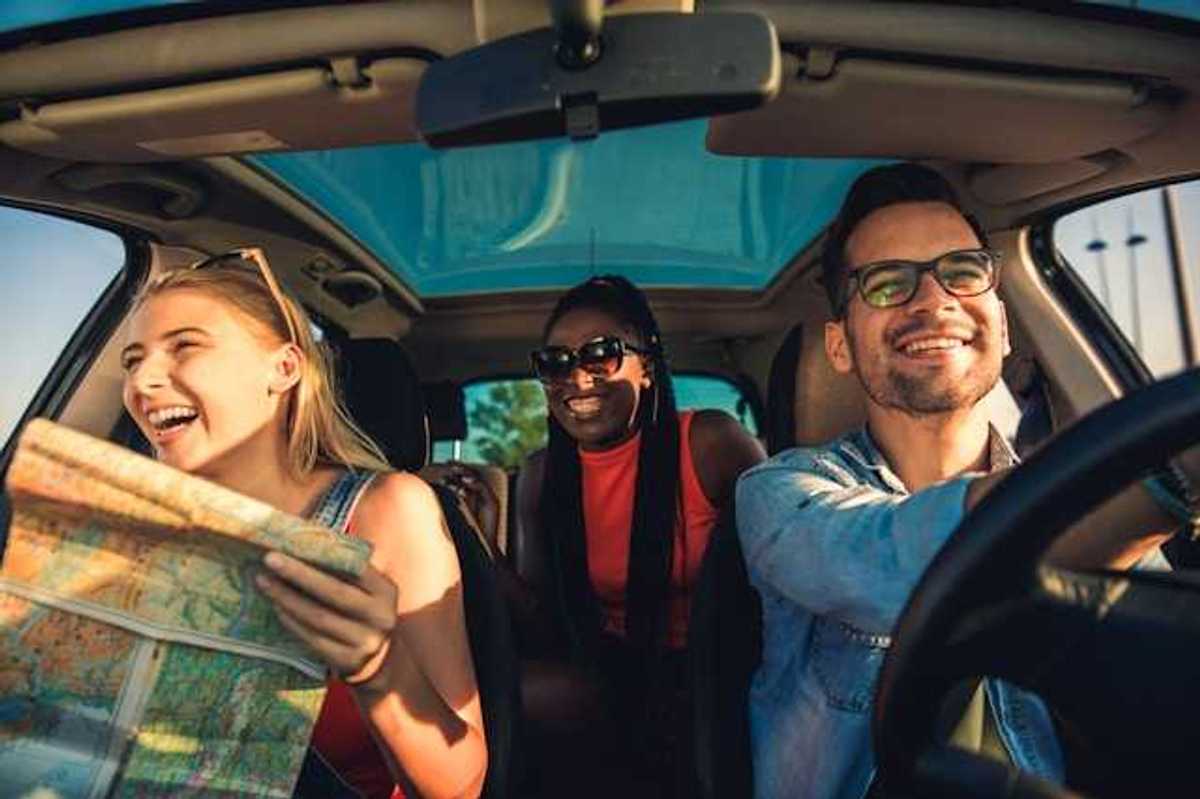 A view of the interior of a car with three laughing people, one of whom is looking at a map