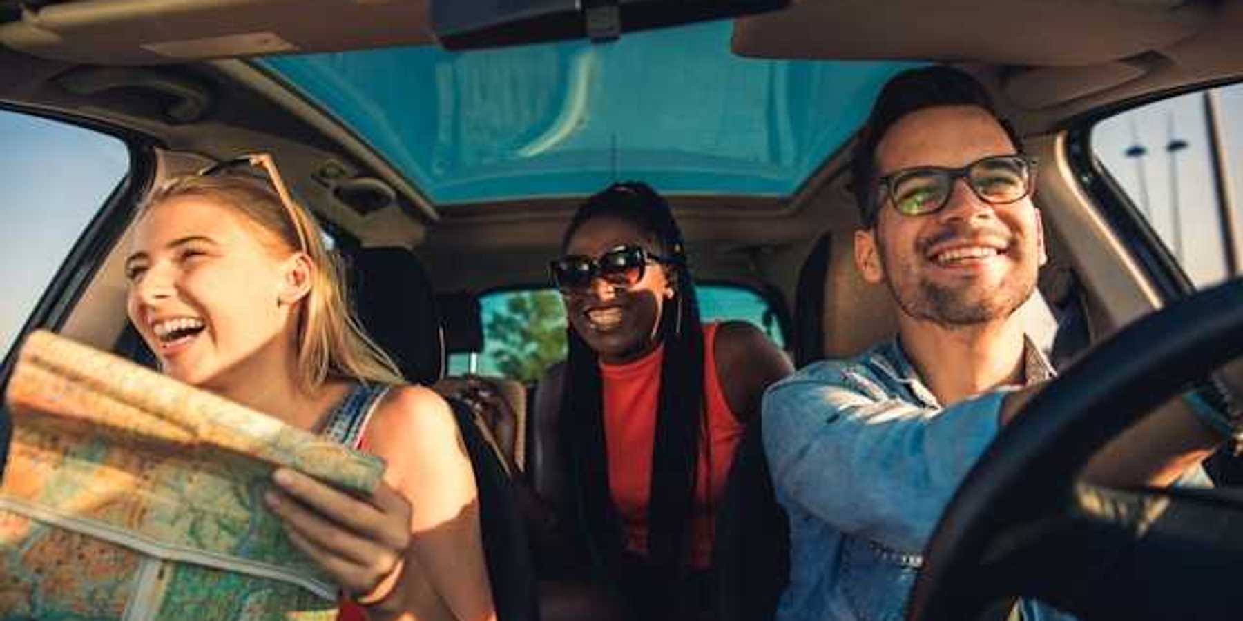 A view of the interior of a car with three laughing people, one of whom is looking at a map