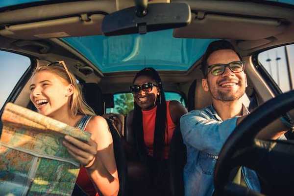 A view of the interior of a car with three laughing people, one of whom is looking at a map