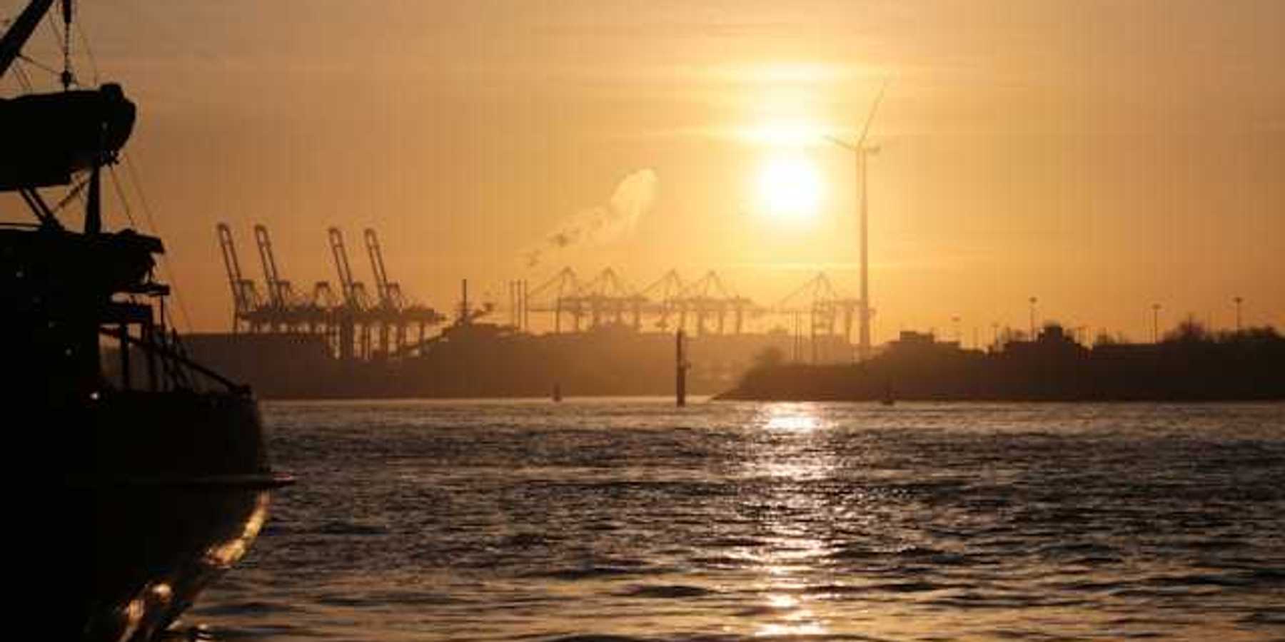 A view of water and ships at sunset with a wind turbine in the background