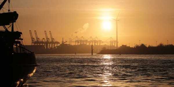 A view of water and ships at sunset with a wind turbine in the background