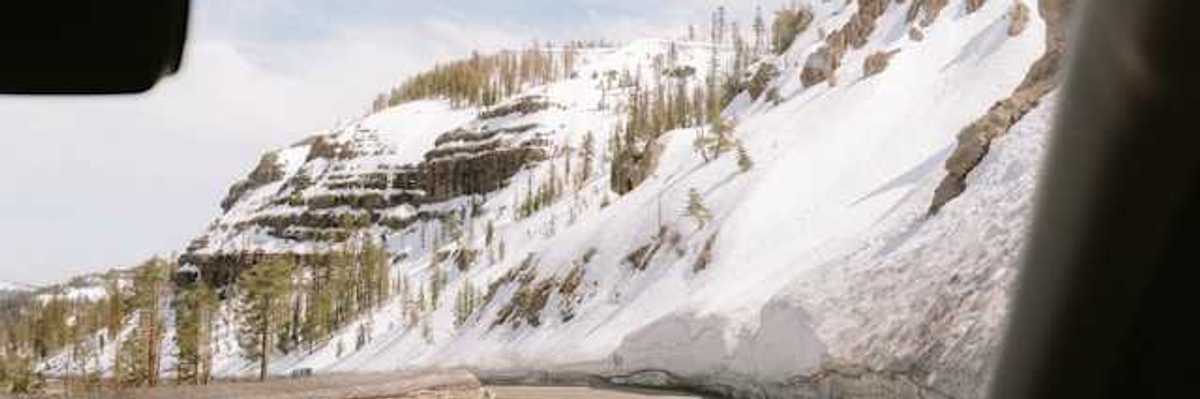 A view out of a car at a mountain road with snowy hillsides