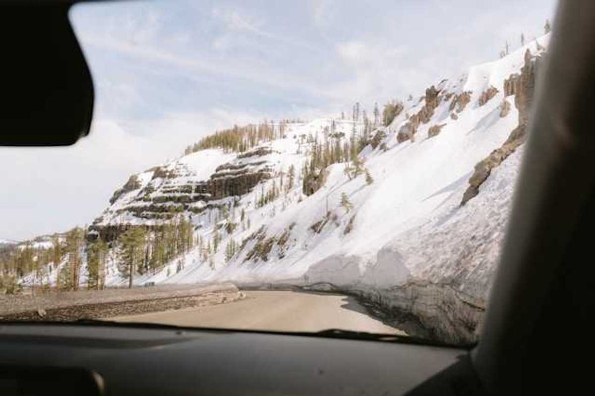 A view out of a car at a mountain road with snowy hillsides