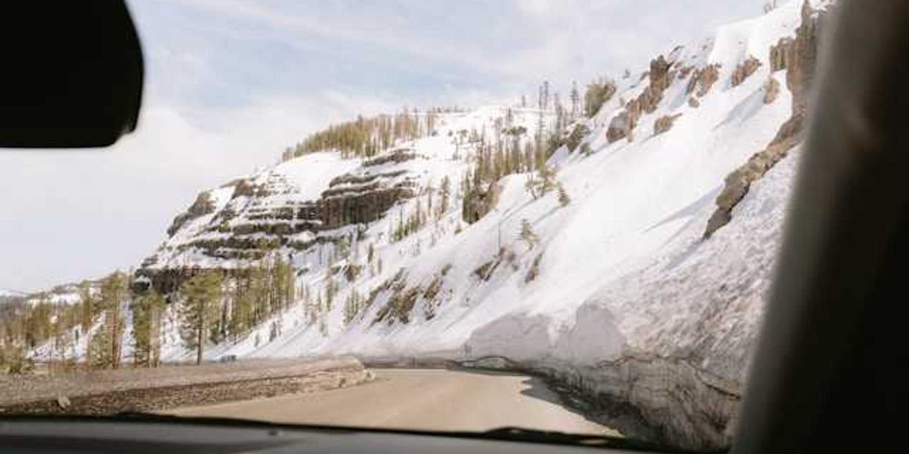 A view out of a car at a mountain road with snowy hillsides