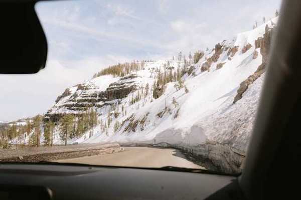 A view out of a car at a mountain road with snowy hillsides