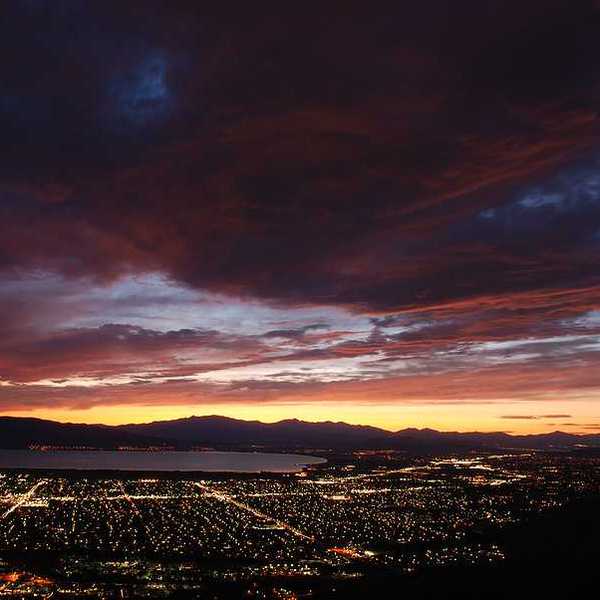 A view over a darkened valley with the lights of houses and a lake in the background