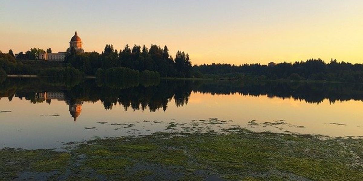 A view over water of the capitol building in Olympia, Washington with a yellow sunset in background.