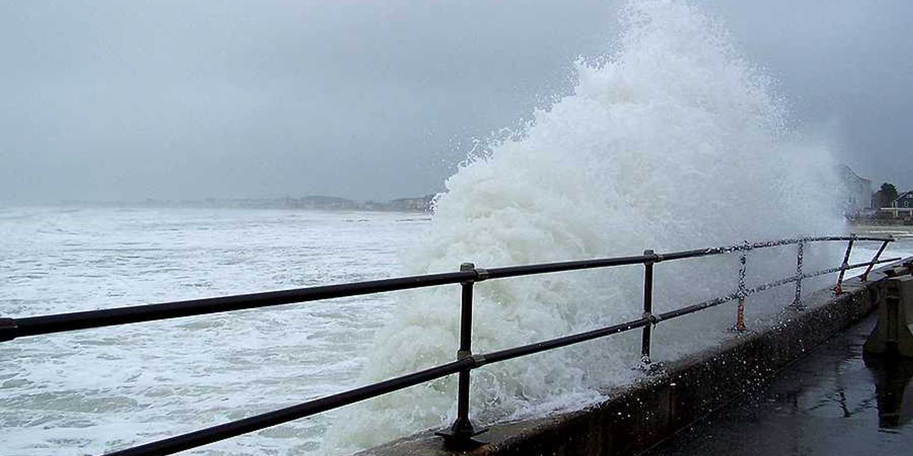 A wave coming up against a fenced sea wall during a storm