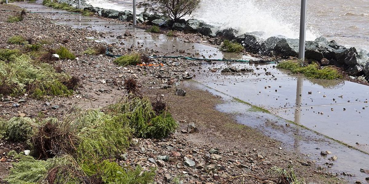 A wave cresting a stone barrier and flowing across a sidewalk.