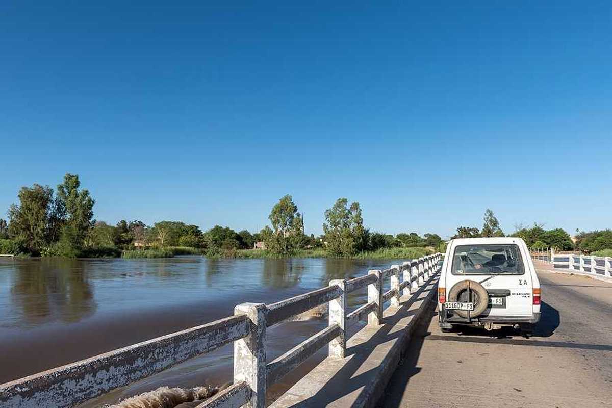 A white car parked on a bridge with rising flood waters beneath it