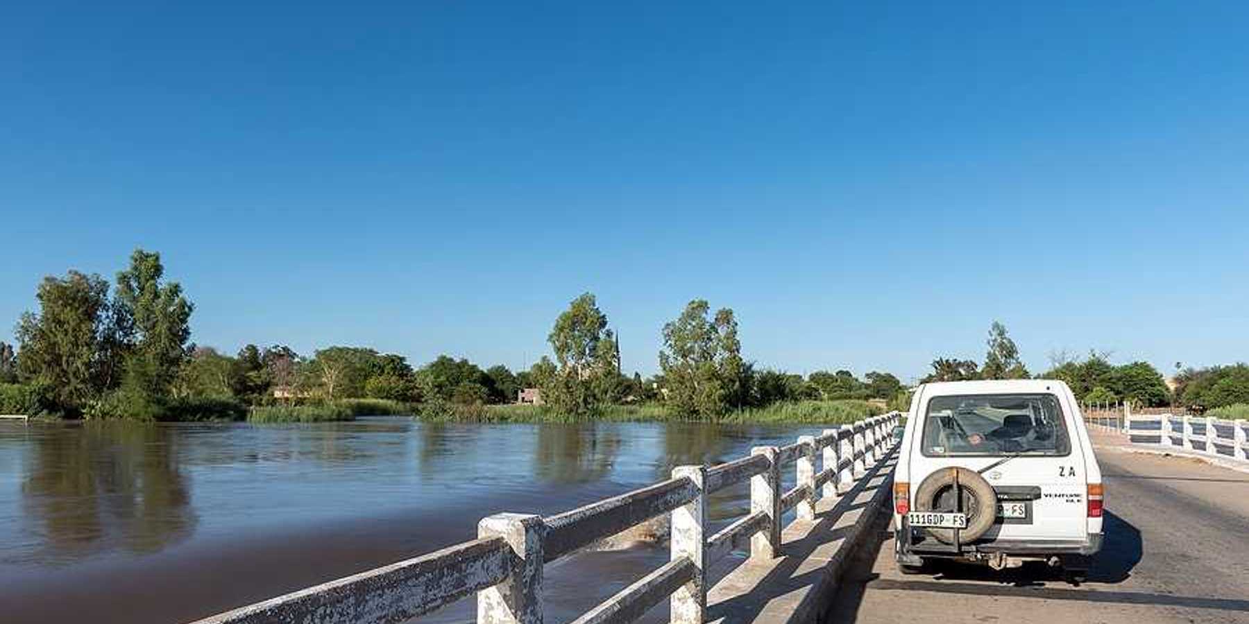 A white car parked on a bridge with rising flood waters beneath it