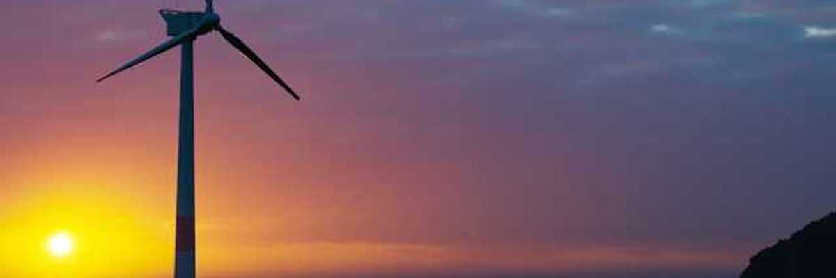 A wind turbine silhouetted against the setting sun