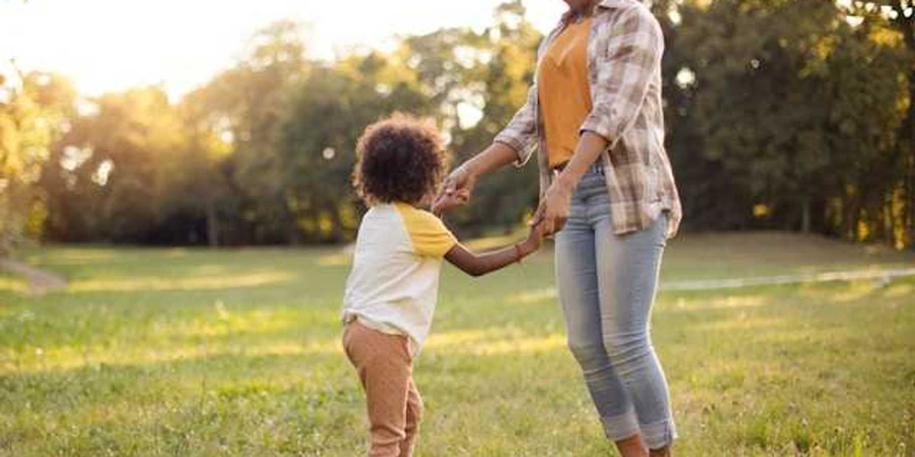 A woman and a child holding hands and dancing in a field