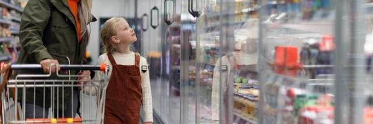 A woman and child standing in front of grocery store refrigerators