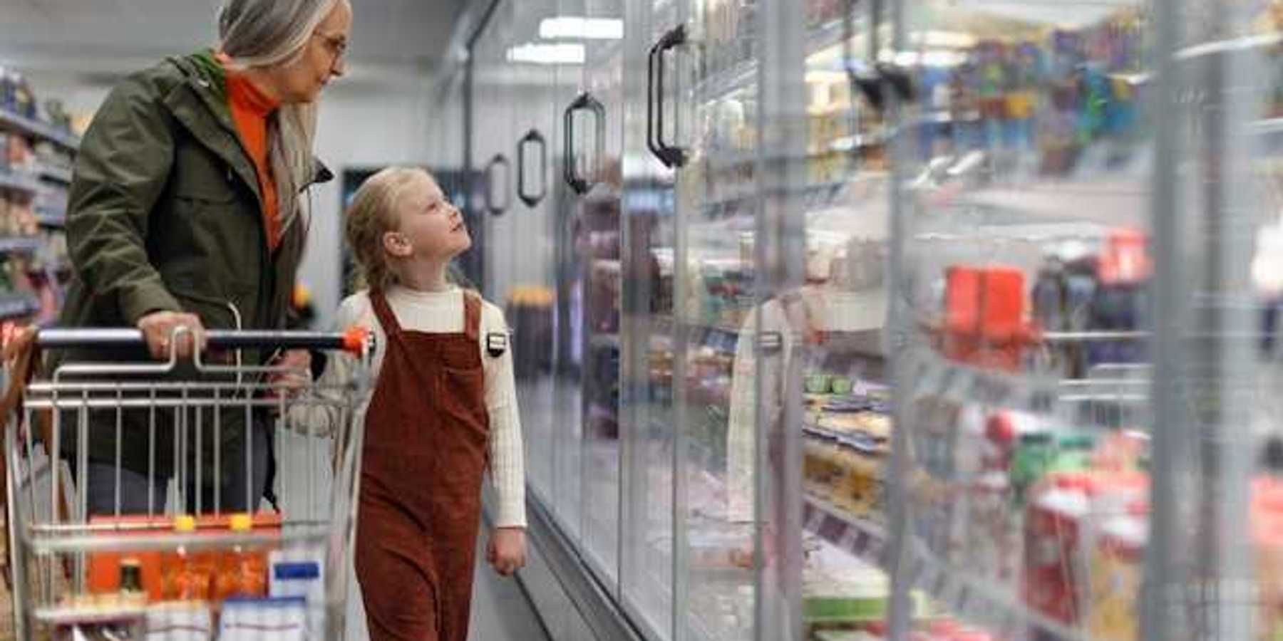 A woman and child standing in front of grocery store refrigerators