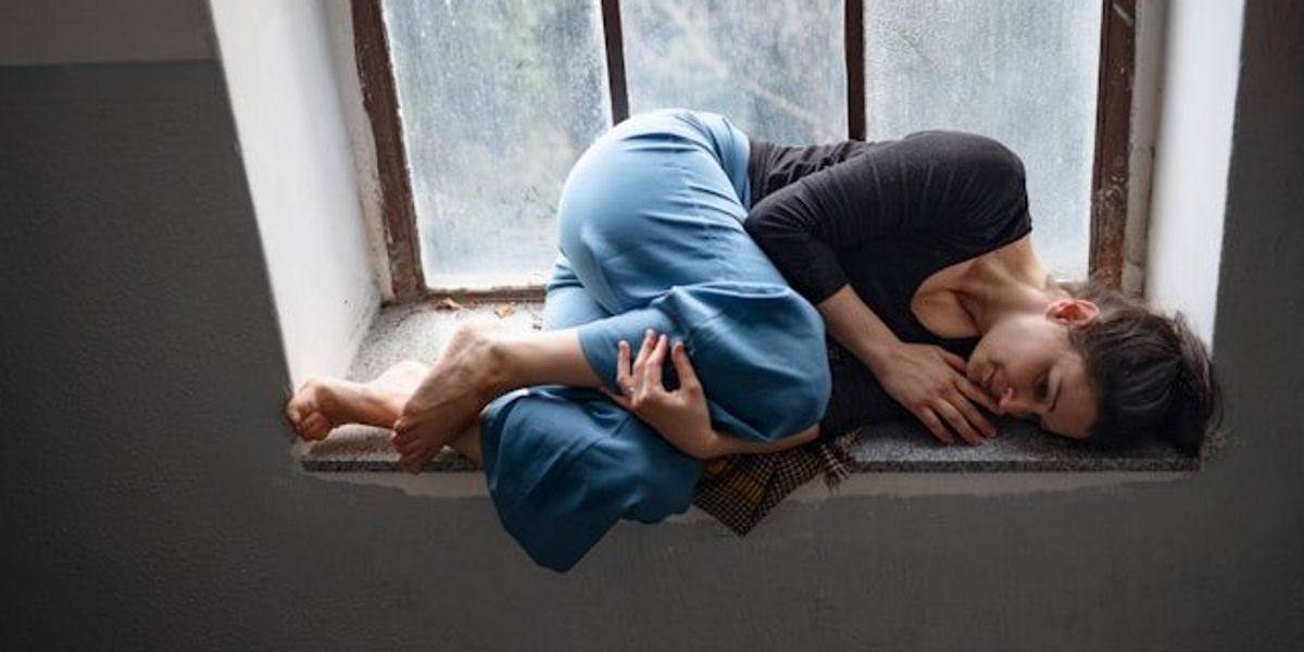 A woman curled in a fetal position in front of a window.