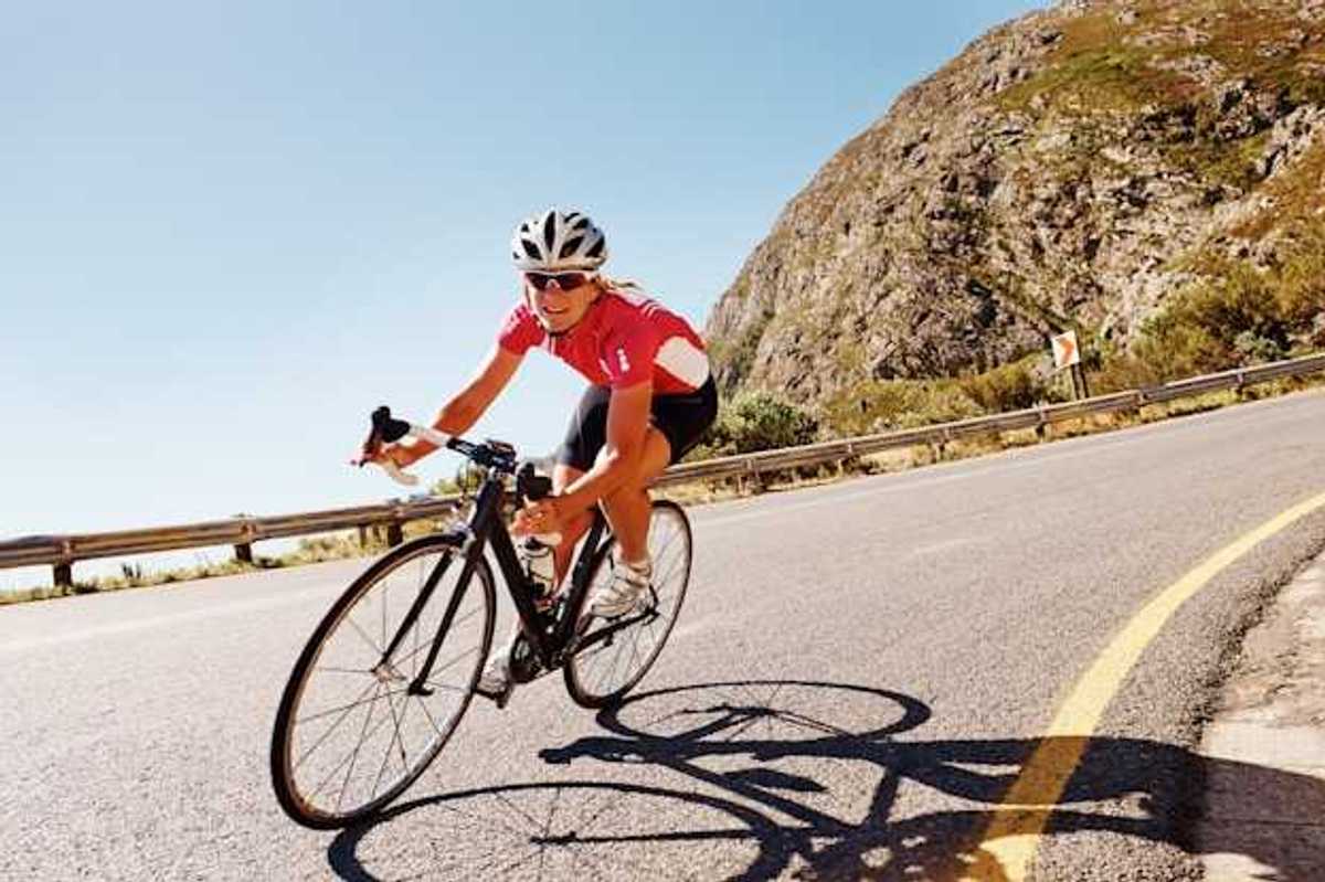 A woman cycling down a road in the sunshine with a red bike jersey on