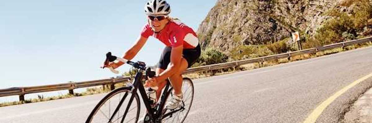 A woman cycling down a road in the sunshine with a red bike kit on