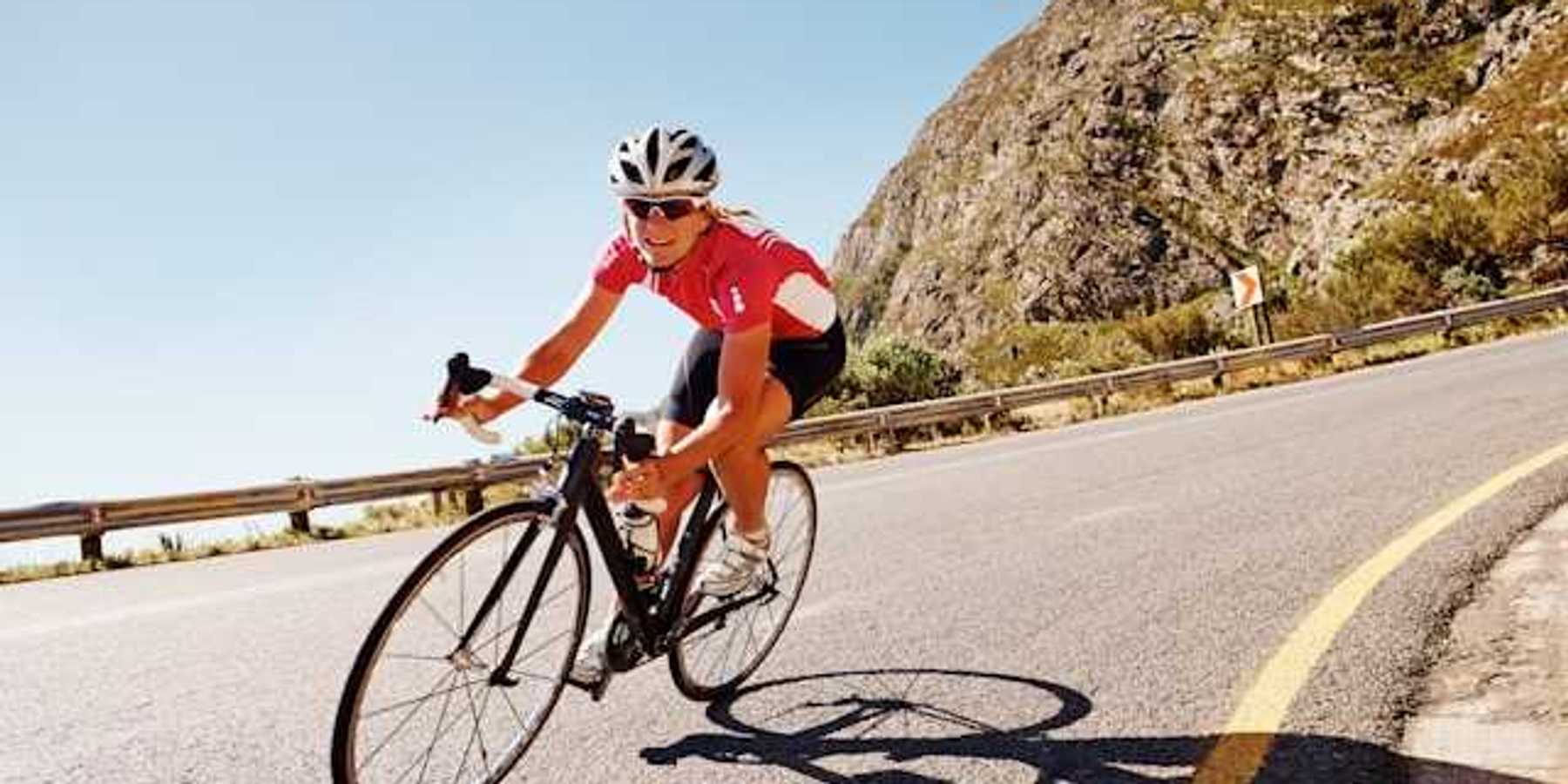 A woman cycling down a road in the sunshine with a red bike kit on