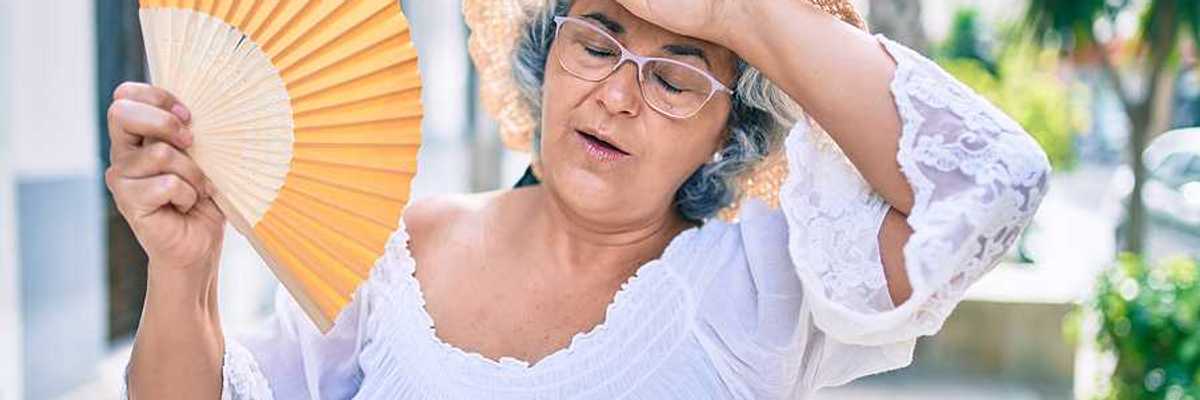 A woman holding a fan and holding her hand to her forehead on a hot day