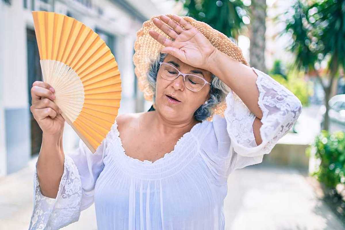 A woman holding a fan and holding her hand to her forehead on a hot day