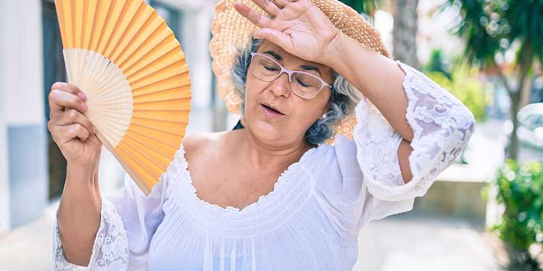 A woman holding a fan and holding her hand to her forehead on a hot day