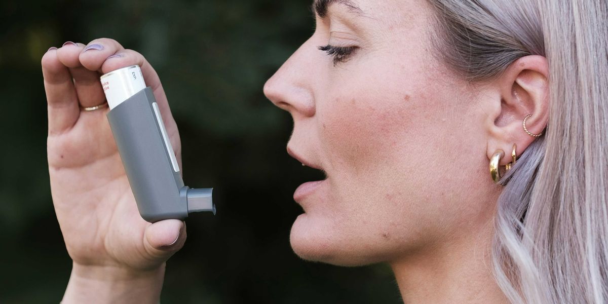 A woman holding an inhaler up to her face.