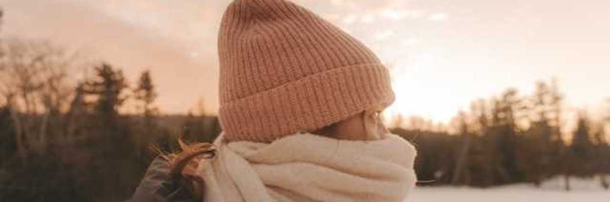 A woman in a snowy lanscape wearing a hat and scarf bundled against the cold weather