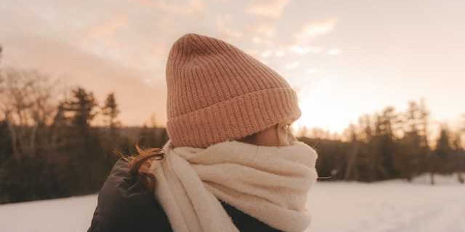 A woman in a snowy lanscape wearing a hat and scarf bundled against the cold weather